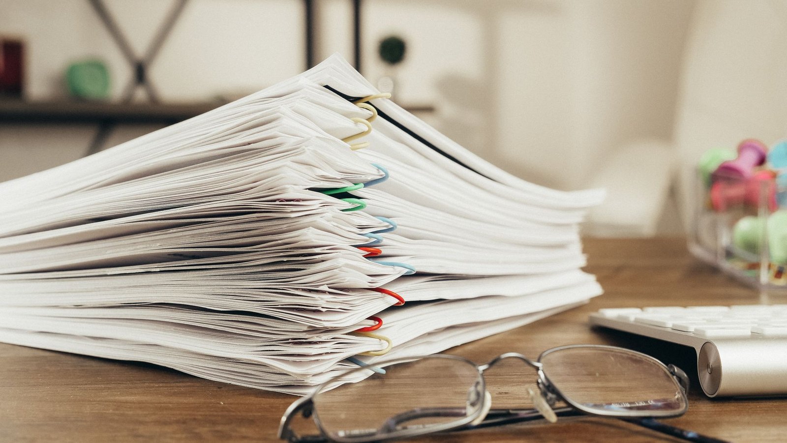 Stack of papers on a desk beside a pair of glasses